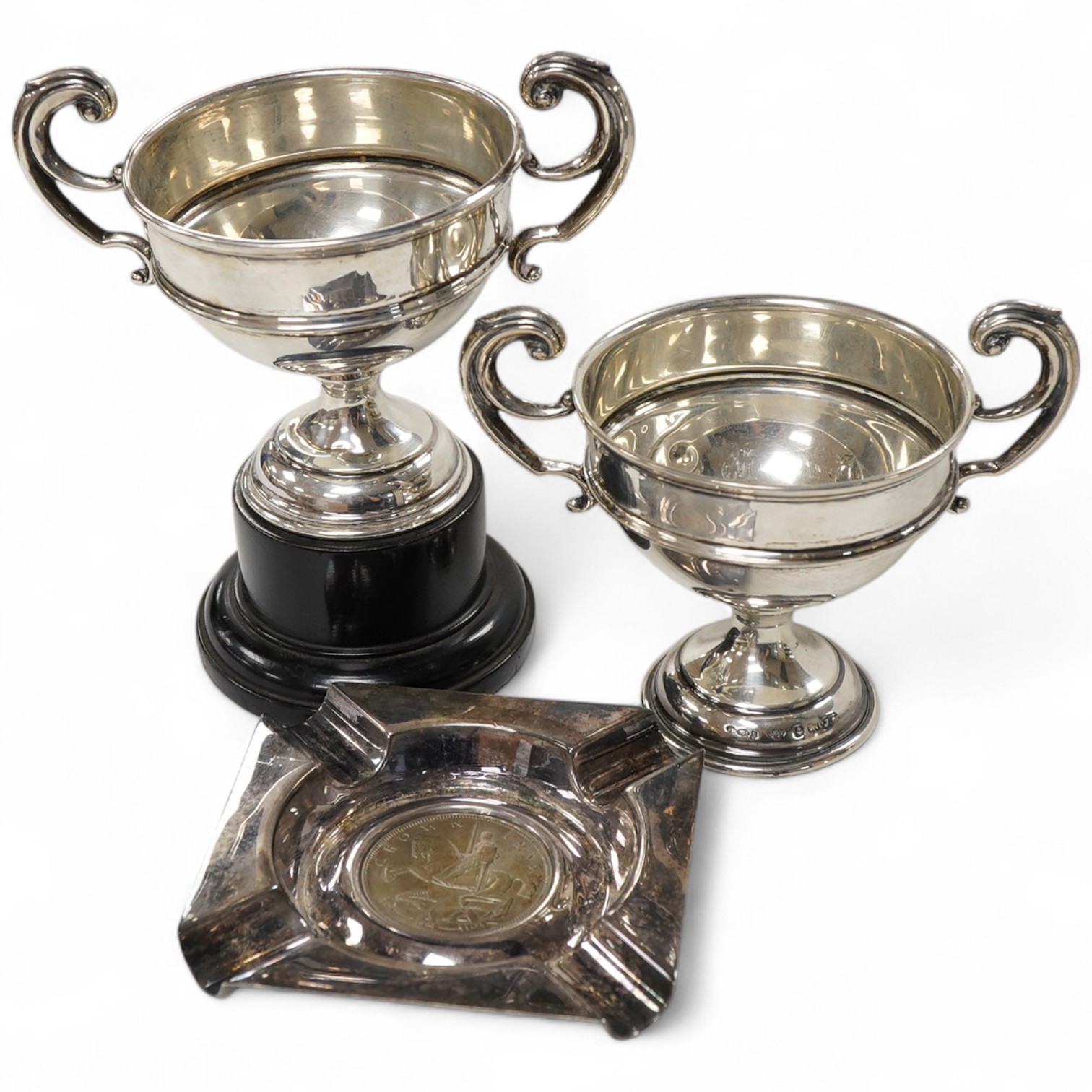 A pair of George V small silver two handled trophy cups by J W Tiptaft & Son Ltd, Birmingham, 1933, height 10cm, one with plinth, together with a George V silver ashtray with inset coin base.